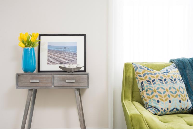 A green coach, pattern pillow, picture frame and side table.